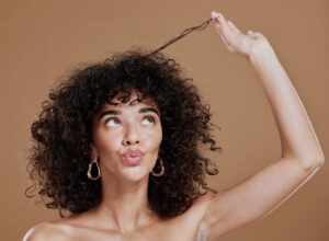 Tricologia capilar: mulher cacheada segura e observa mecha de cabelo acima da cabeça